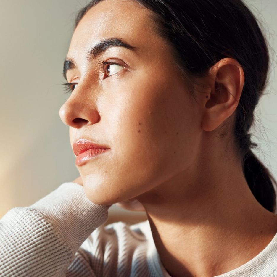 A woman in a brown sweater is sitting in a chair with her hand on her chin.