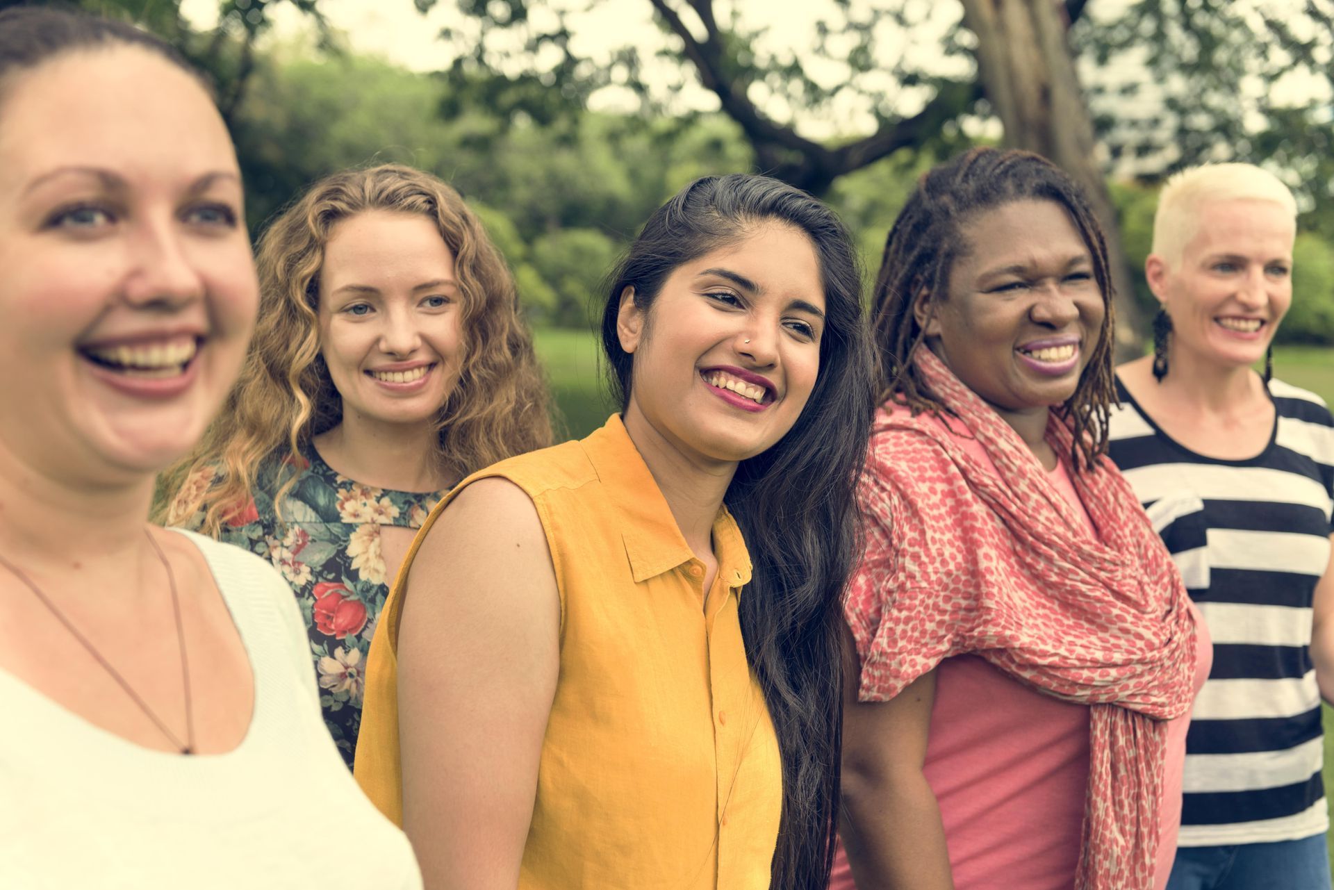 A group of women are standing next to each other in a park and smiling.
