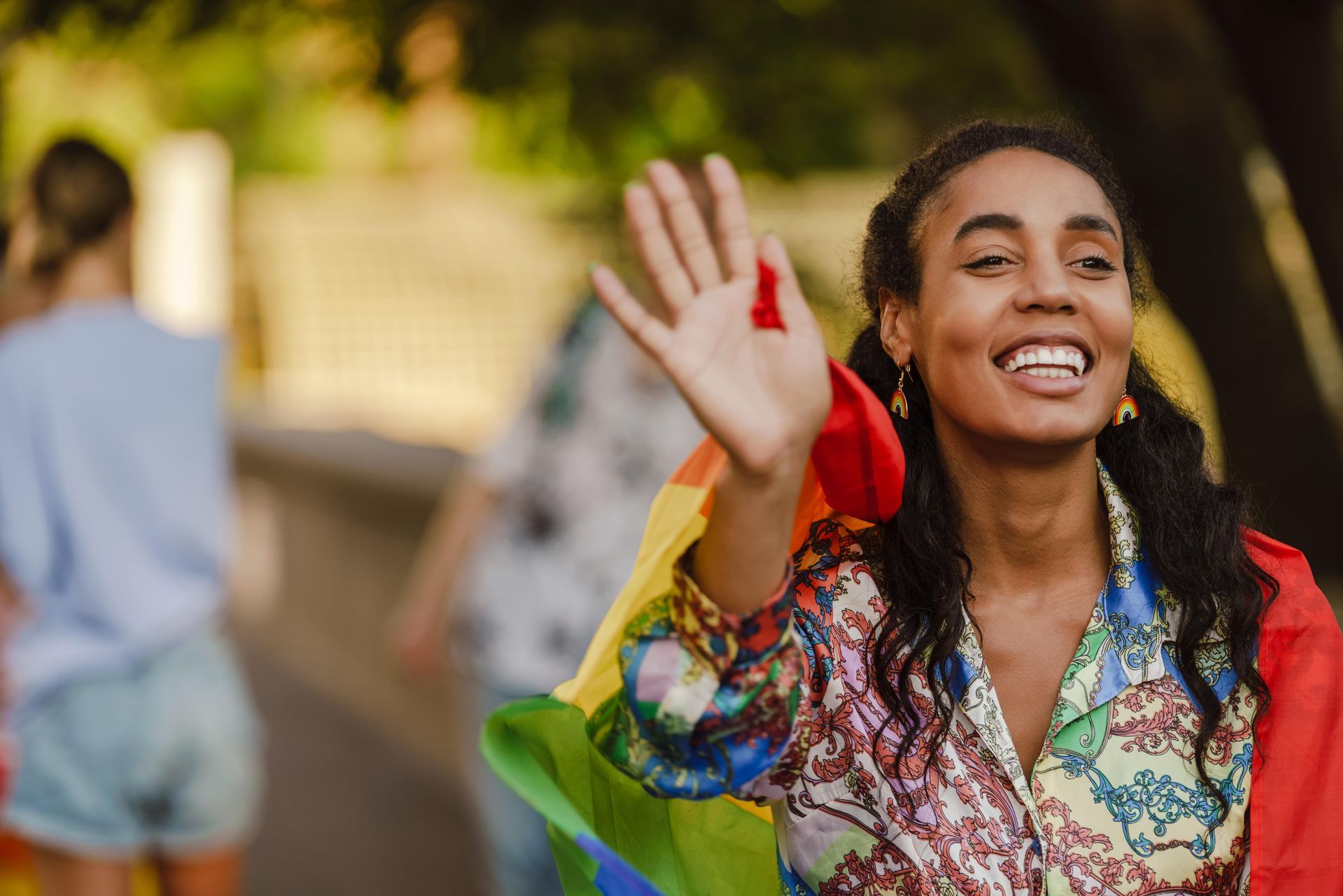A woman is holding a rainbow flag and waving at the camera.