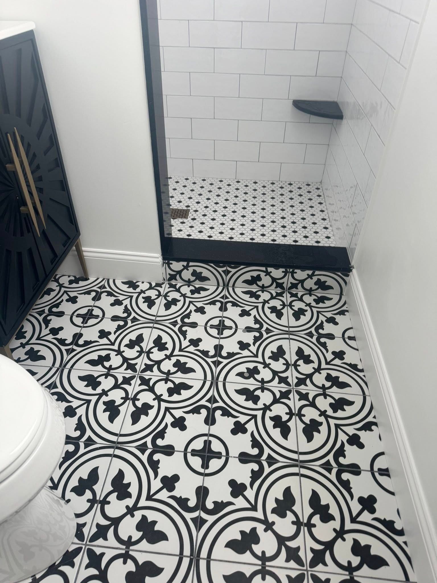 Black-and-white tiled bathroom with patterned floor, white shower area, and toilet visible on the left.