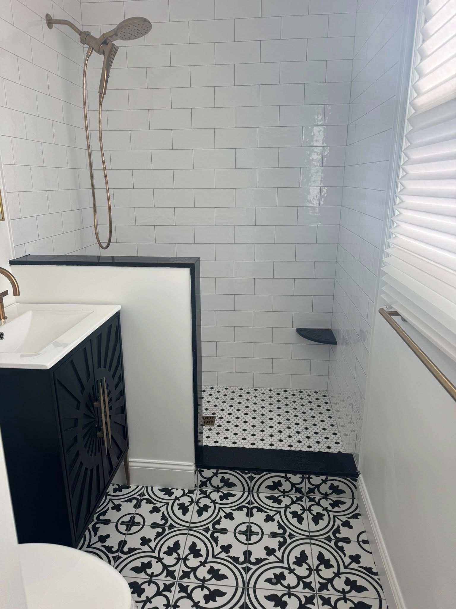 Small tiled bathroom with a shower, black vanity, patterned floor, and window blinds.