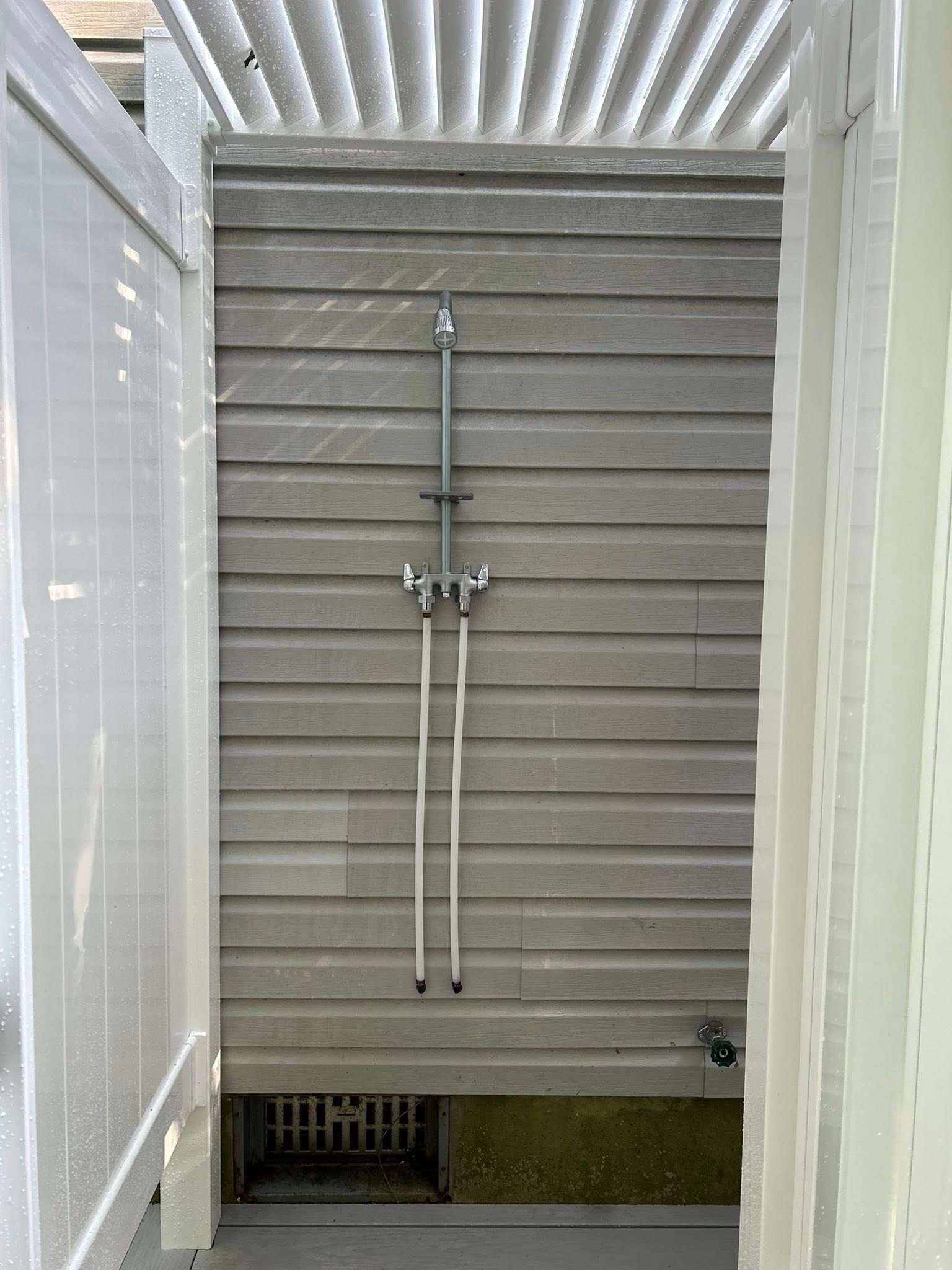 Shower stall with gray walls, chrome shower fixtures, and a corrugated roof overhead