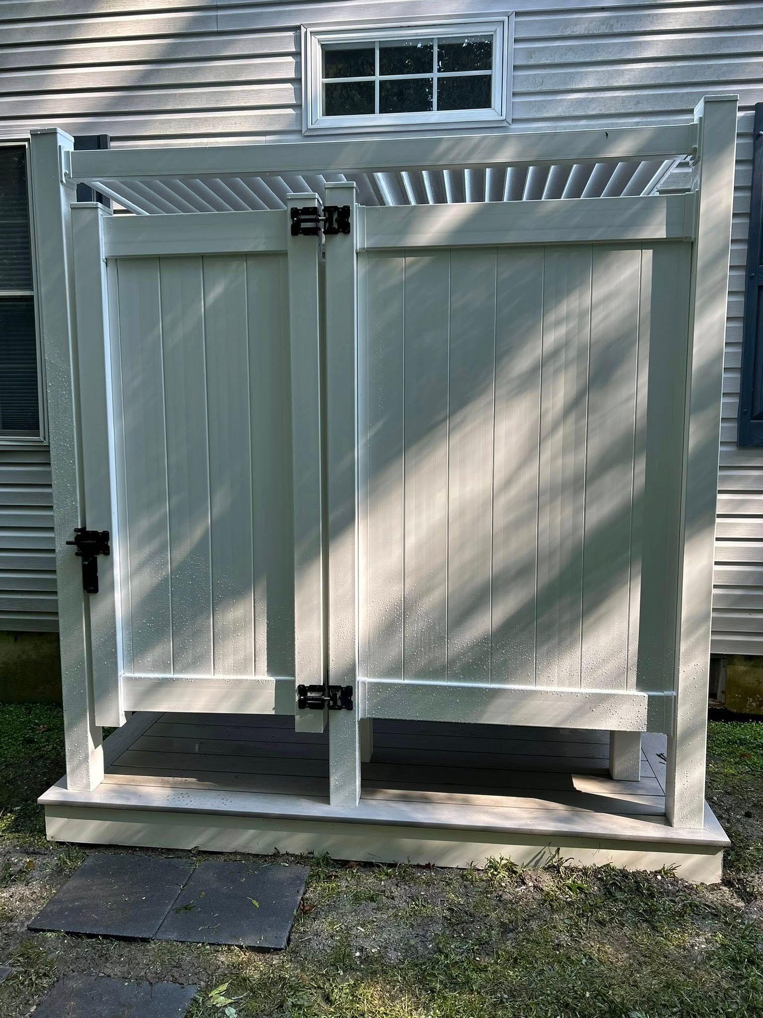 White double privacy gate under a slatted pergola beside a house, with a small window above.