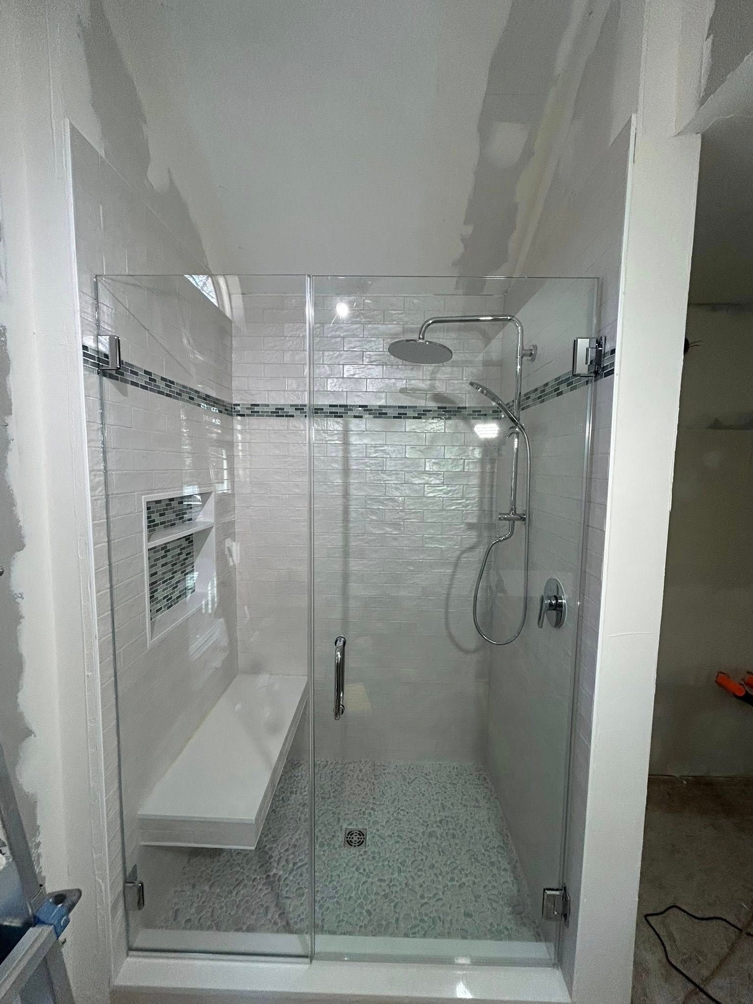 Modern white-tiled shower with glass door, bench, niche shelf, and handheld showerhead