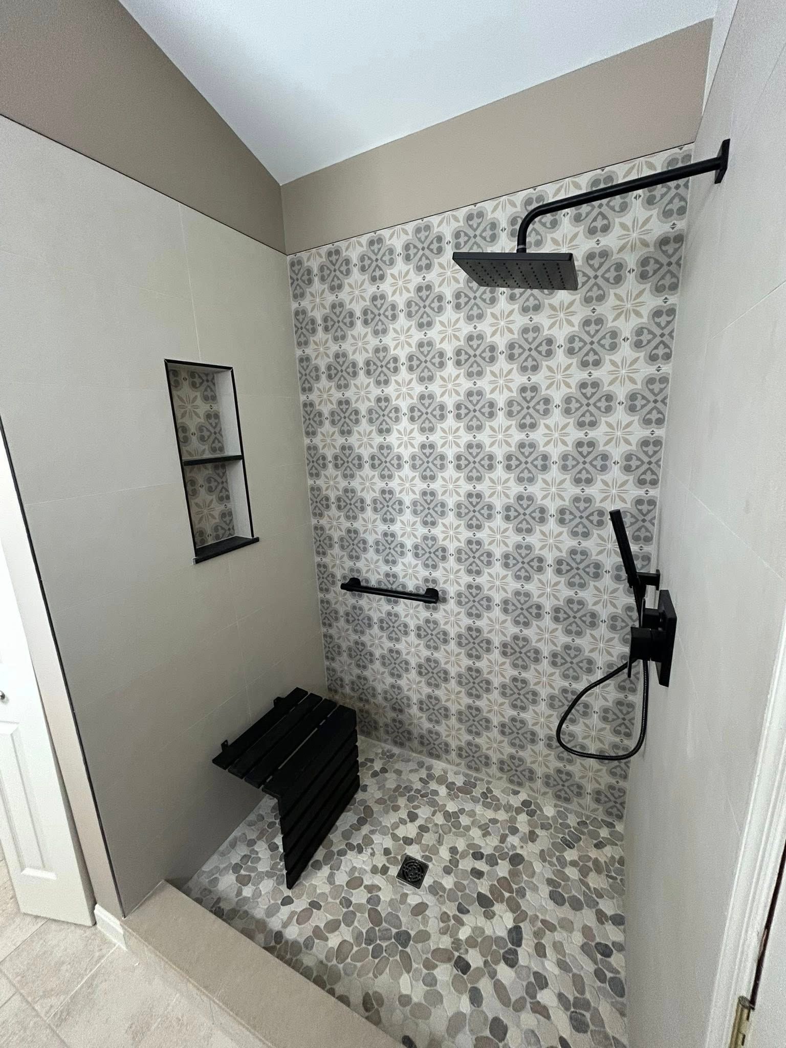Small tiled walk-in shower with black fixtures, shower bench, and patterned wall tiles.