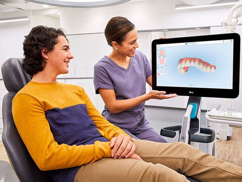 A dentist shows a teen patient a 3D model of teeth on a screen in a dental office.