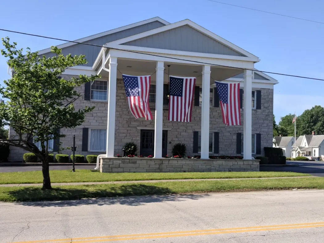 Large stone building with white columns and American flags hanging from the front entrance.