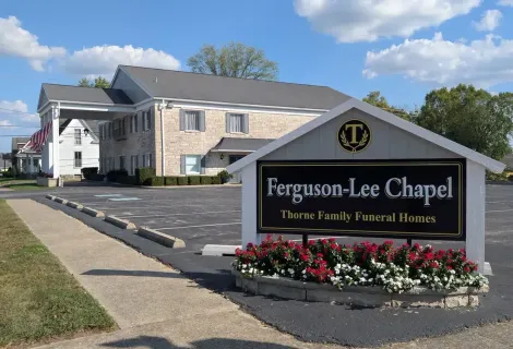 Ferguson-Lee Chapel funeral home sign beside a beige building and flower bed under a blue sky