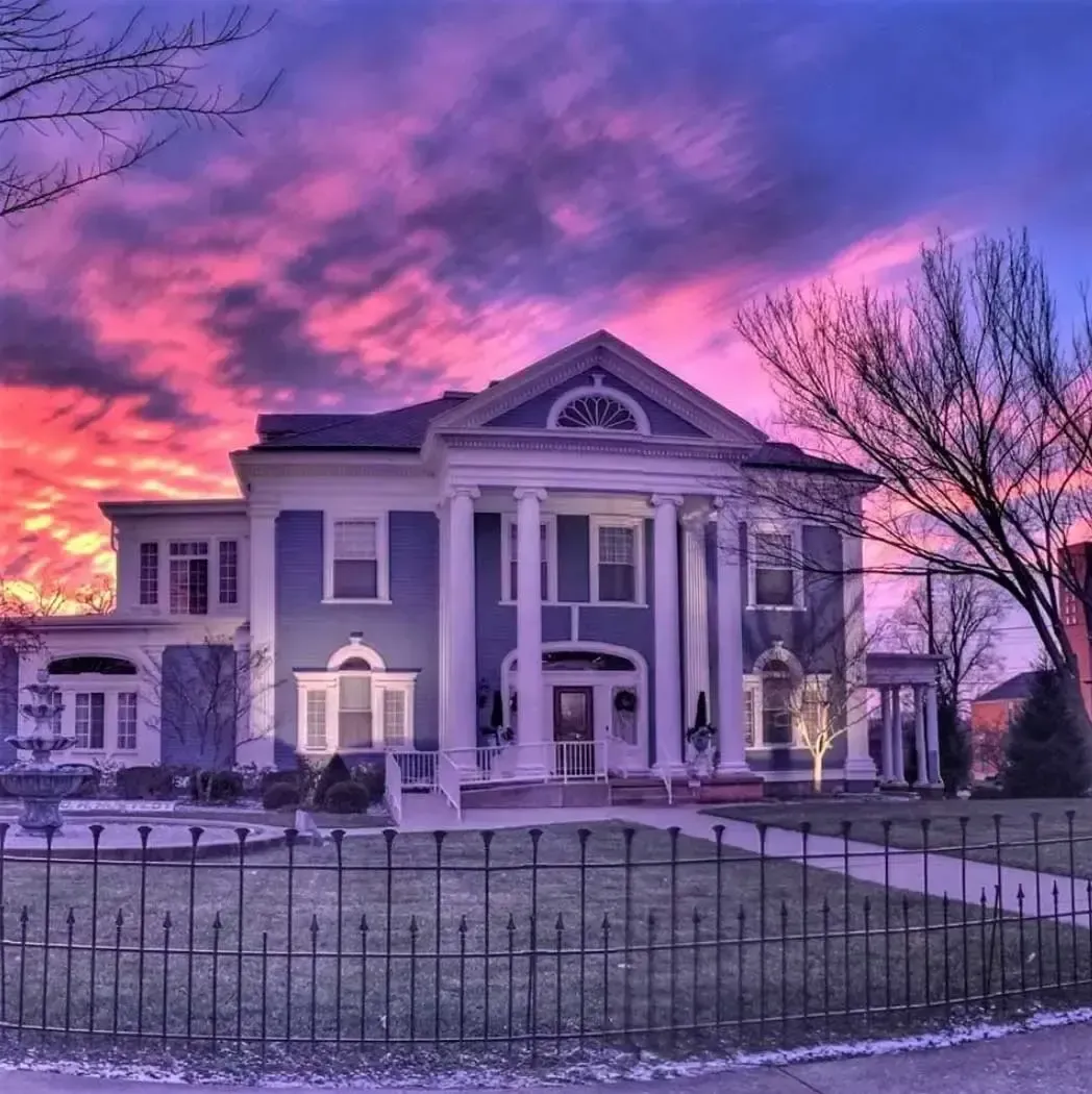 Grand historic mansion with a columned facade beneath a vivid pink-purple sunset sky