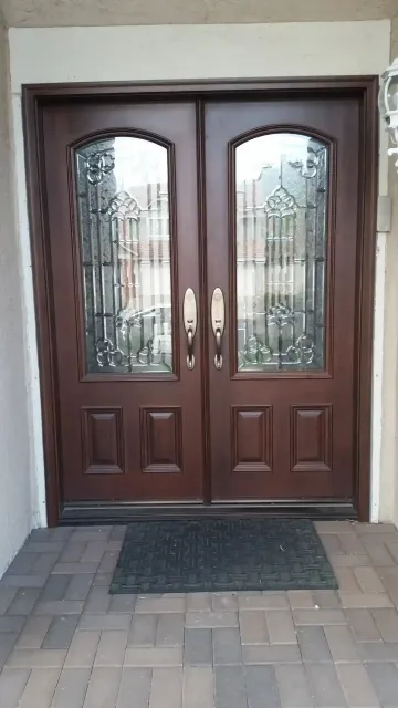 Brown double front doors with glass panes and brass handles at an entrance with a doormat