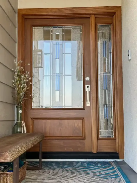 Wooden front door with glass panels, sidelights, bench, and patterned rug in an entryway