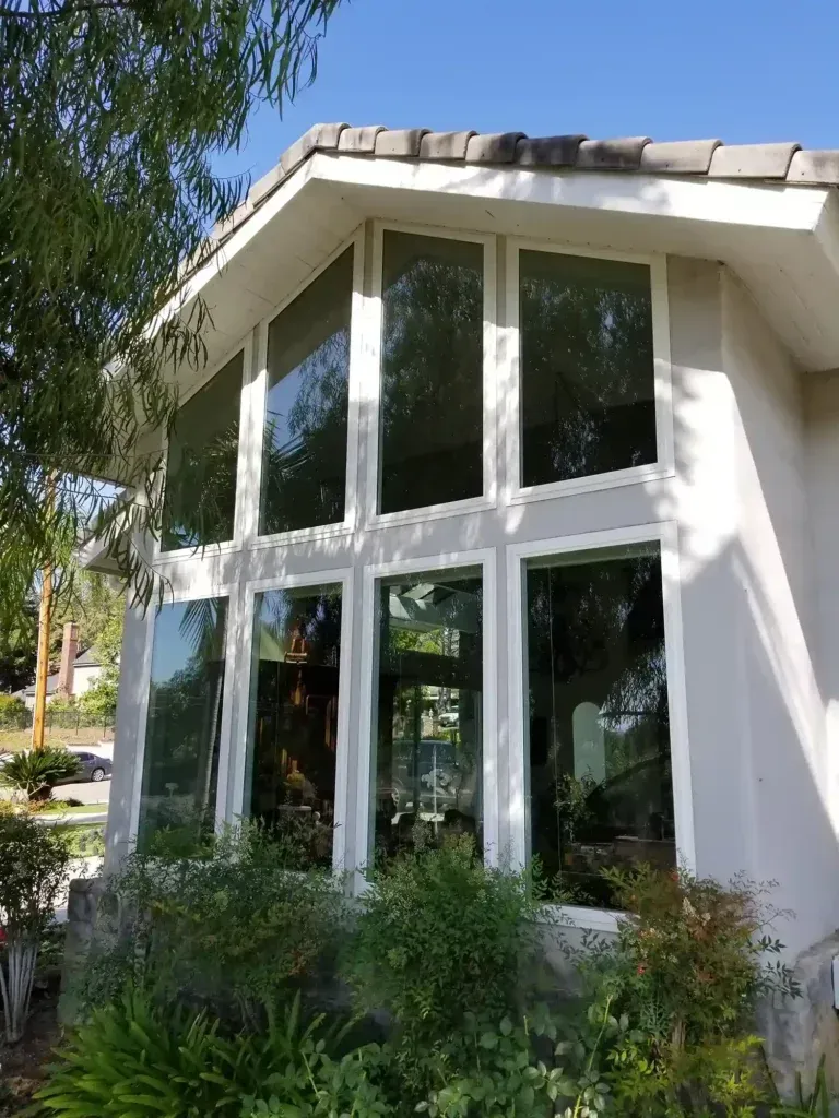 White house exterior with large windows, sloped roof, and lush green landscaping in front