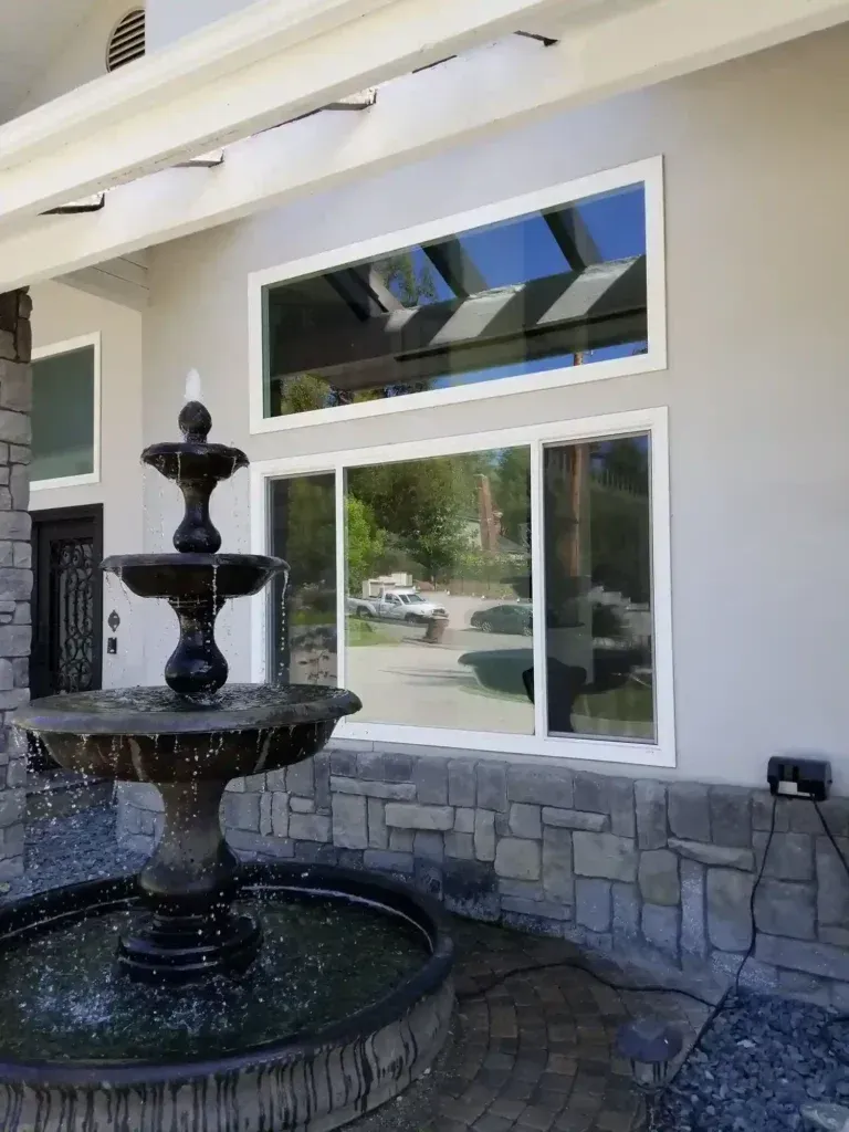 Black tiered fountain beside a large window on a stone patio outside a beige building