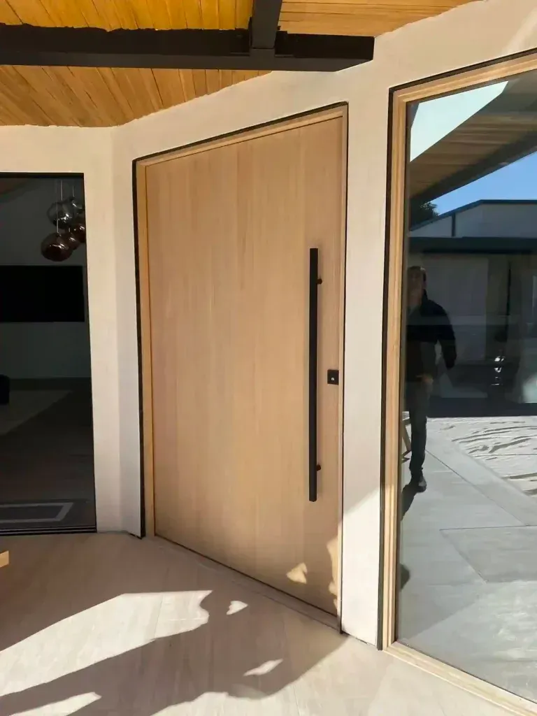 Modern entryway with a light wood door, glass sidelight, and sunlit tiled floor.