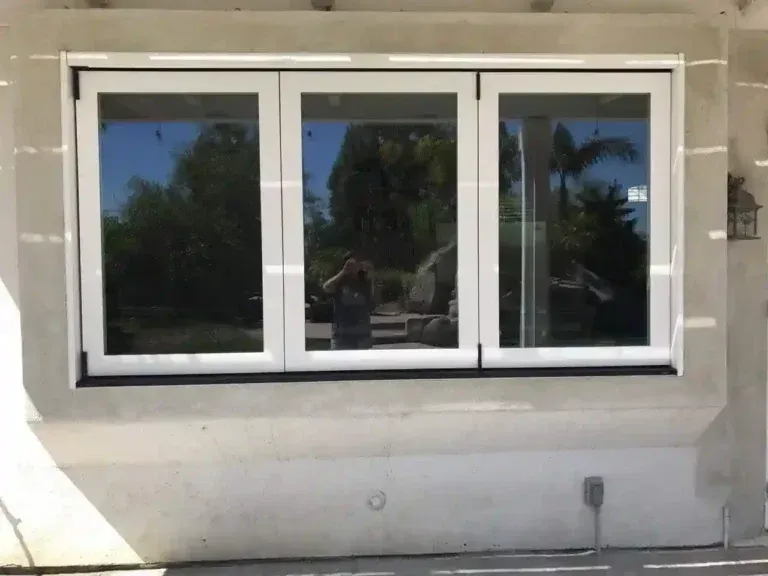 White-framed three-pane window on a beige exterior wall reflecting palm trees and the sky