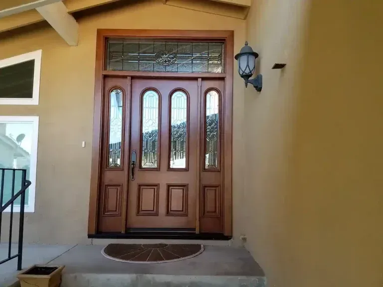 Front entry with a wooden double door, sidelights, and a wall-mounted lantern under a covered porch.