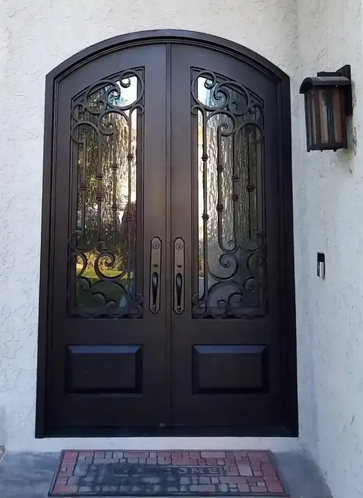 Black double front door with decorative glass panels beside a wall lantern and welcome mat