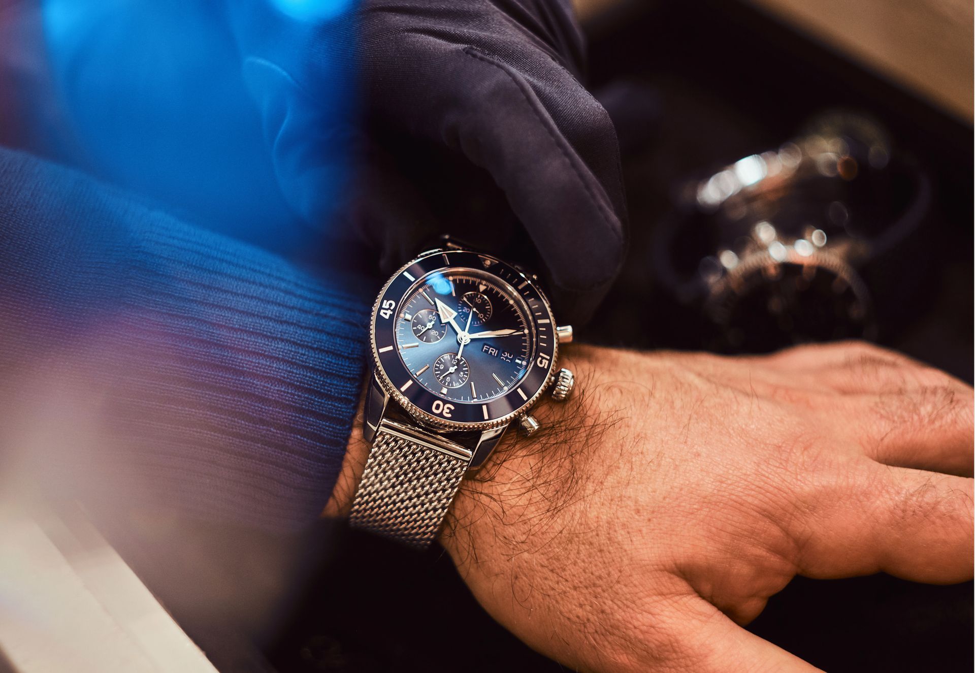 Il polso di una persona con un orologio di lusso. Quadrante blu scuro, cinturino argento, guanto nero.