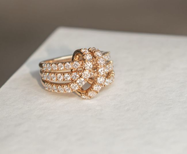 Anello in oro con diamanti, caratterizzato da un motivo a nodo con tre fasce e un nodo centrale ricoperto di diamanti.
