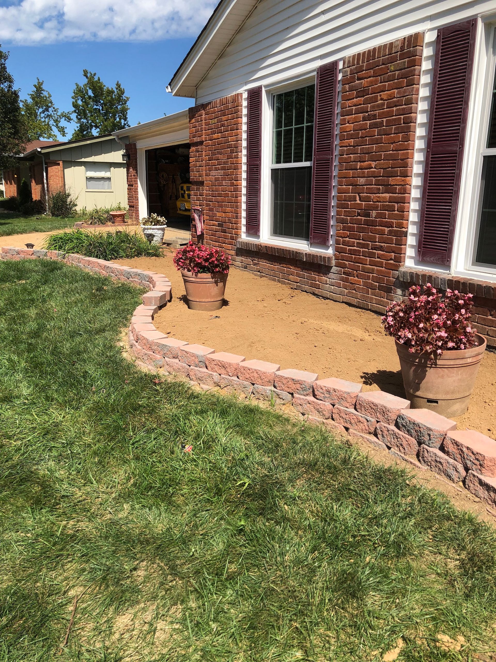 Retaining wall garden bed with plants in front of brick house.