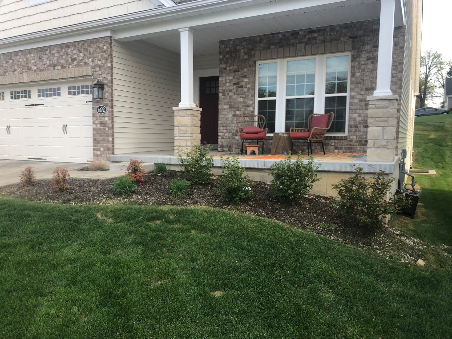 A house with a porch, lawn and garden bed in front of it.