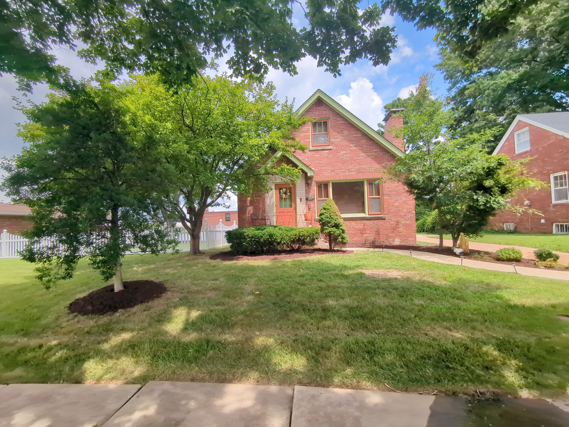 A brick house with a large lawn and trees in front of it.