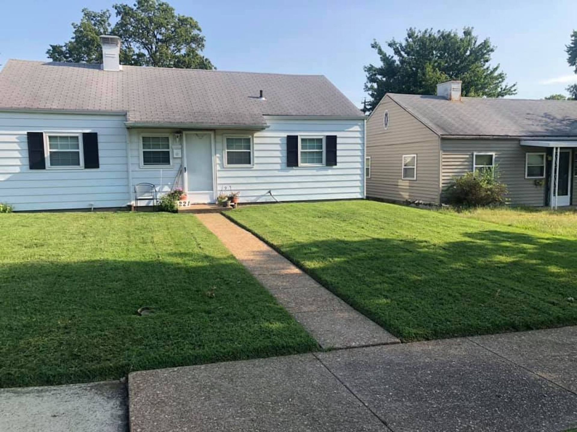 A white house with black shutters with a freshly mowed lawn in front of it.