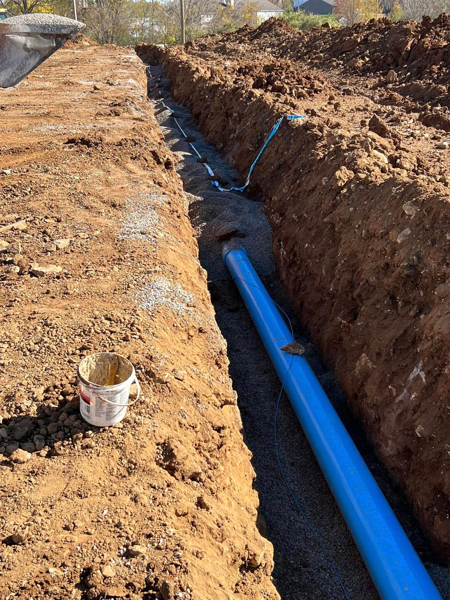 A blue pipe is laying in the dirt next to a bucket.