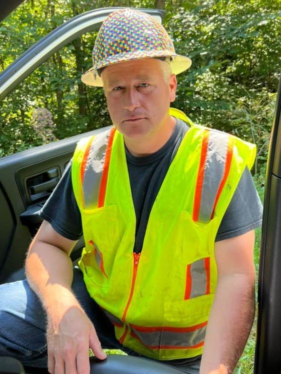 A man wearing a hard hat and a yellow vest is sitting in a car.