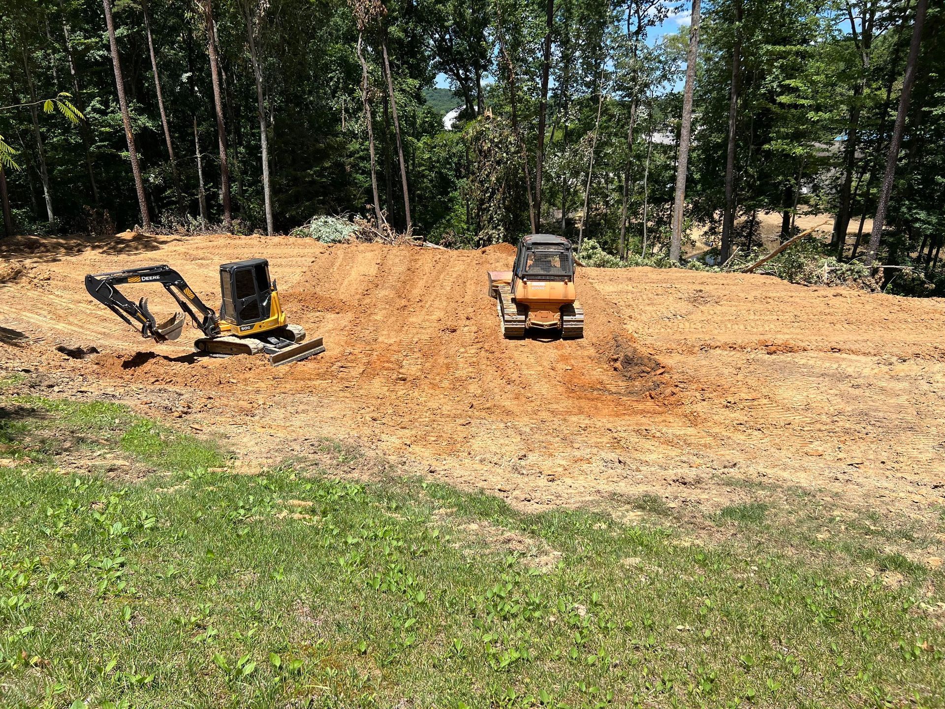 A bulldozer is driving through a dirt field next to a forest.