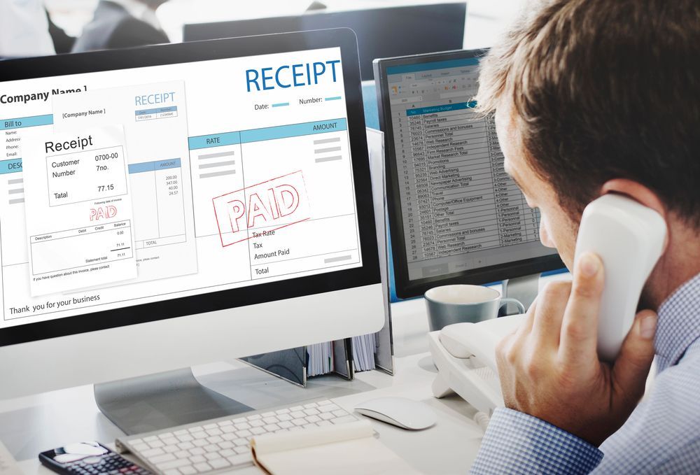 Office worker on phone reviewing a computer screen with invoices marked “RECEIPT” and “PAID”