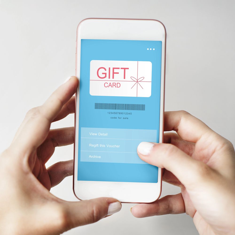 Hands holding a smartphone displaying a blue gift card screen with a red ribbon graphic.