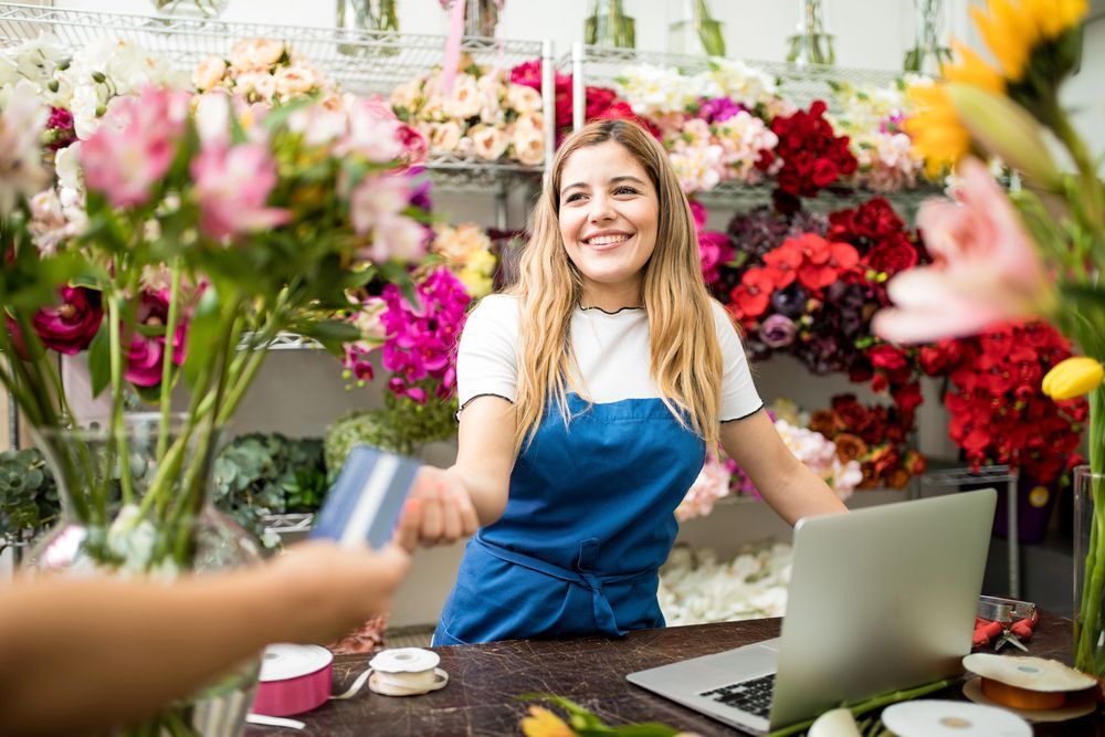 Smiling florist at flower shop counter, with colorful bouquets and a laptop nearby