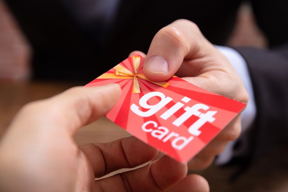 Hands exchanging a red gift card with a gold ribbon design and the words “gift card” on it.