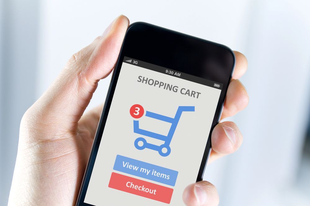 Hand holding smartphone showing shopping cart app with blue cart and red checkout button