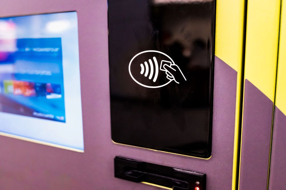 Contactless payment reader on a purple machine with a hand-tap icon and yellow striped side panel