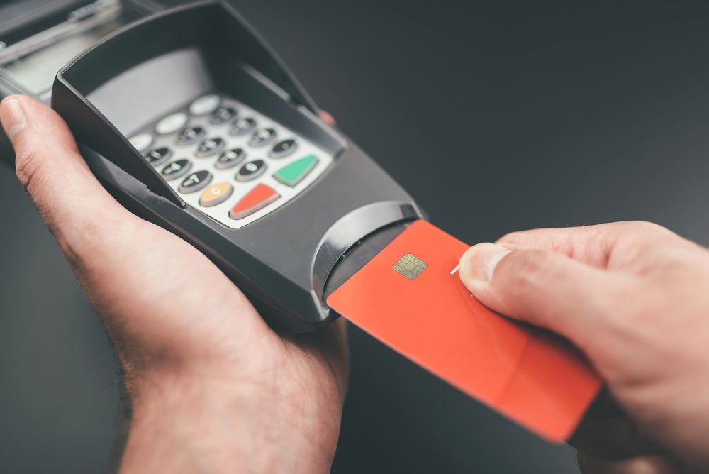 Hands holding a card reader while a red payment card is inserted for contactless payment.