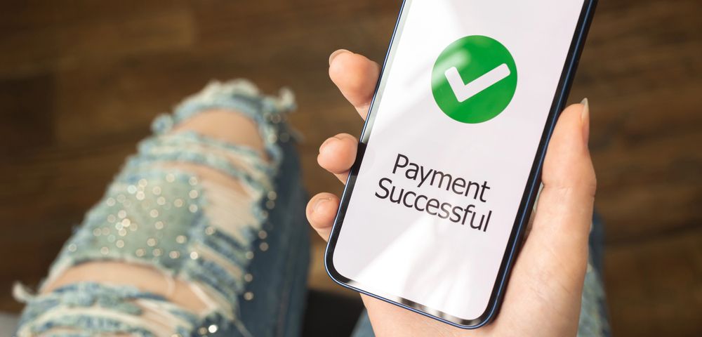 Hand holding smartphone with green checkmark and “Payment Successful” message on screen