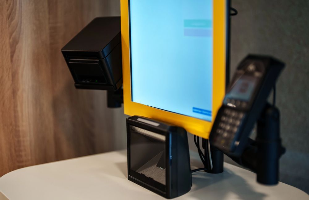 Contactless payment terminal with yellow frame on a counter beside a card reader and receipt printer