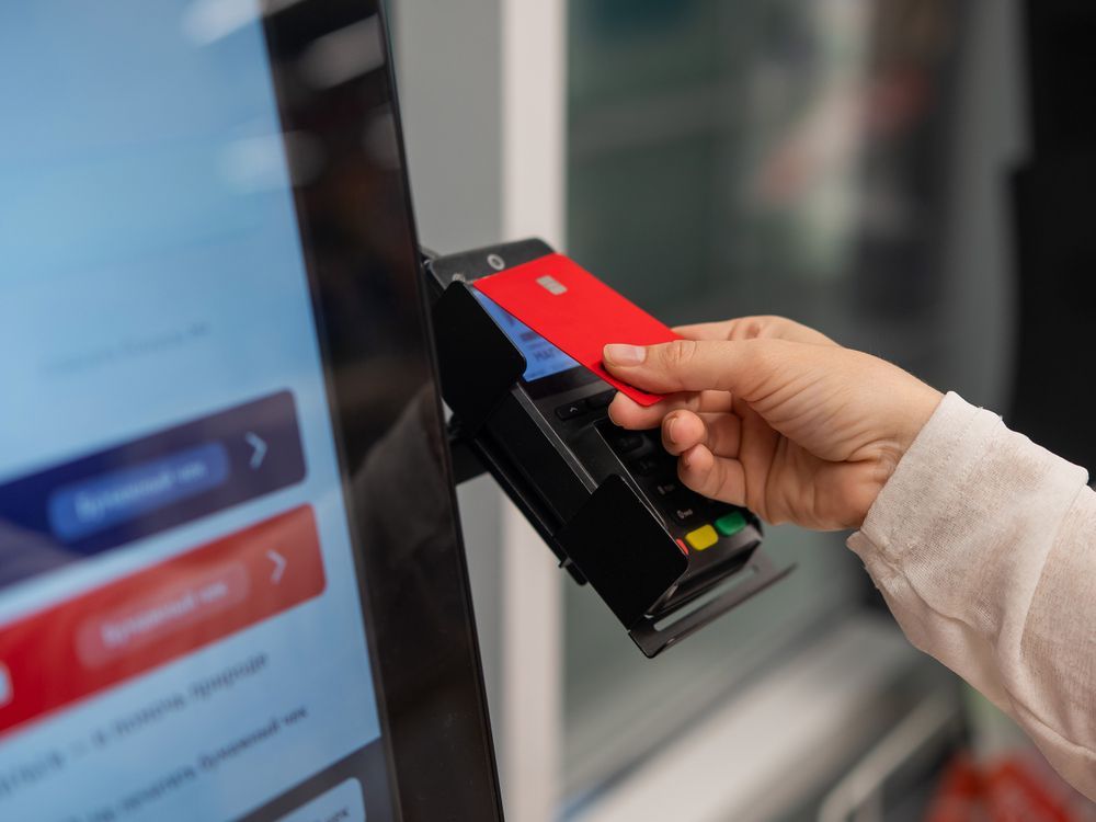 Hand inserting a red card into a payment terminal beside a touchscreen