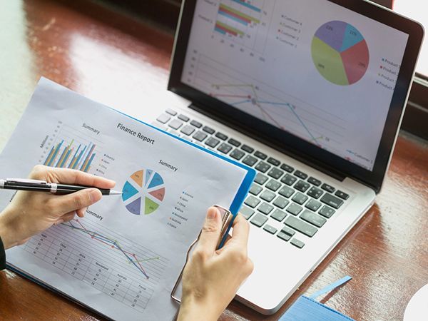 Hands analyzing colorful charts on a tablet beside a laptop with pie charts and graphs
