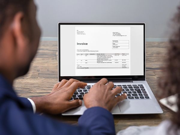 Person typing on a laptop displaying an invoice in a home office
