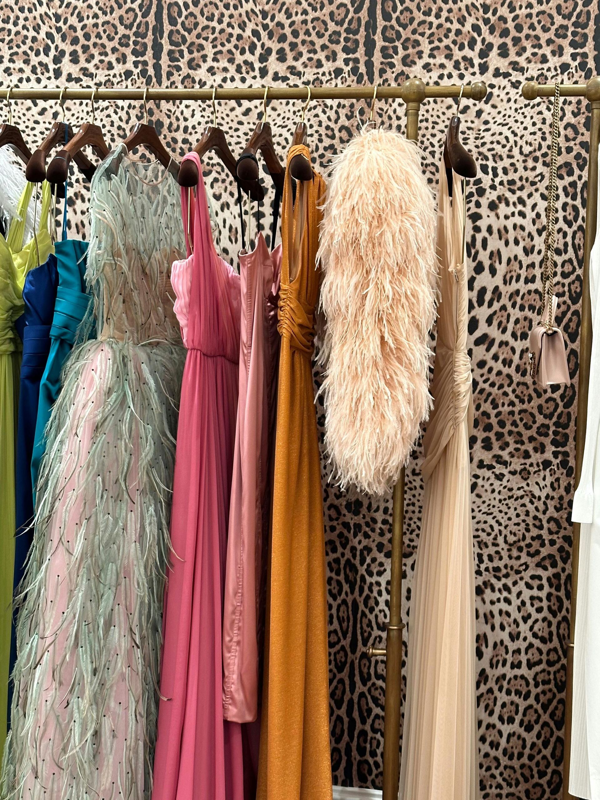 Dresses hanging on a rack against a leopard print wallpaper. Various colors and textures.