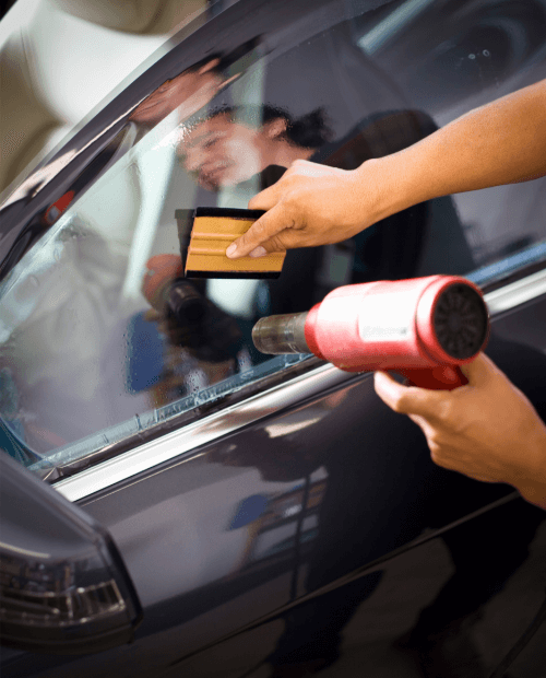 technician applying new window tint film to a car side window during an automotive tint replacement
