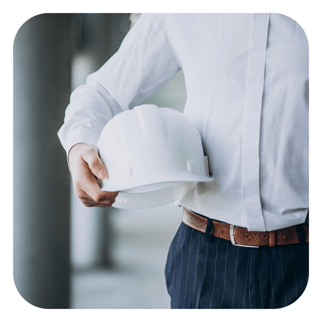 Uma pessoa vestindo uma camisa branca de botões e calças escuras segura um capacete de construção branco ao lado do corpo.