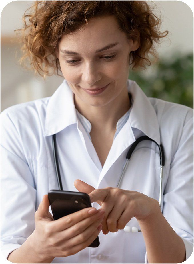 Um profissional de saúde sorridente, de jaleco branco e estetoscópio, usando um smartphone.