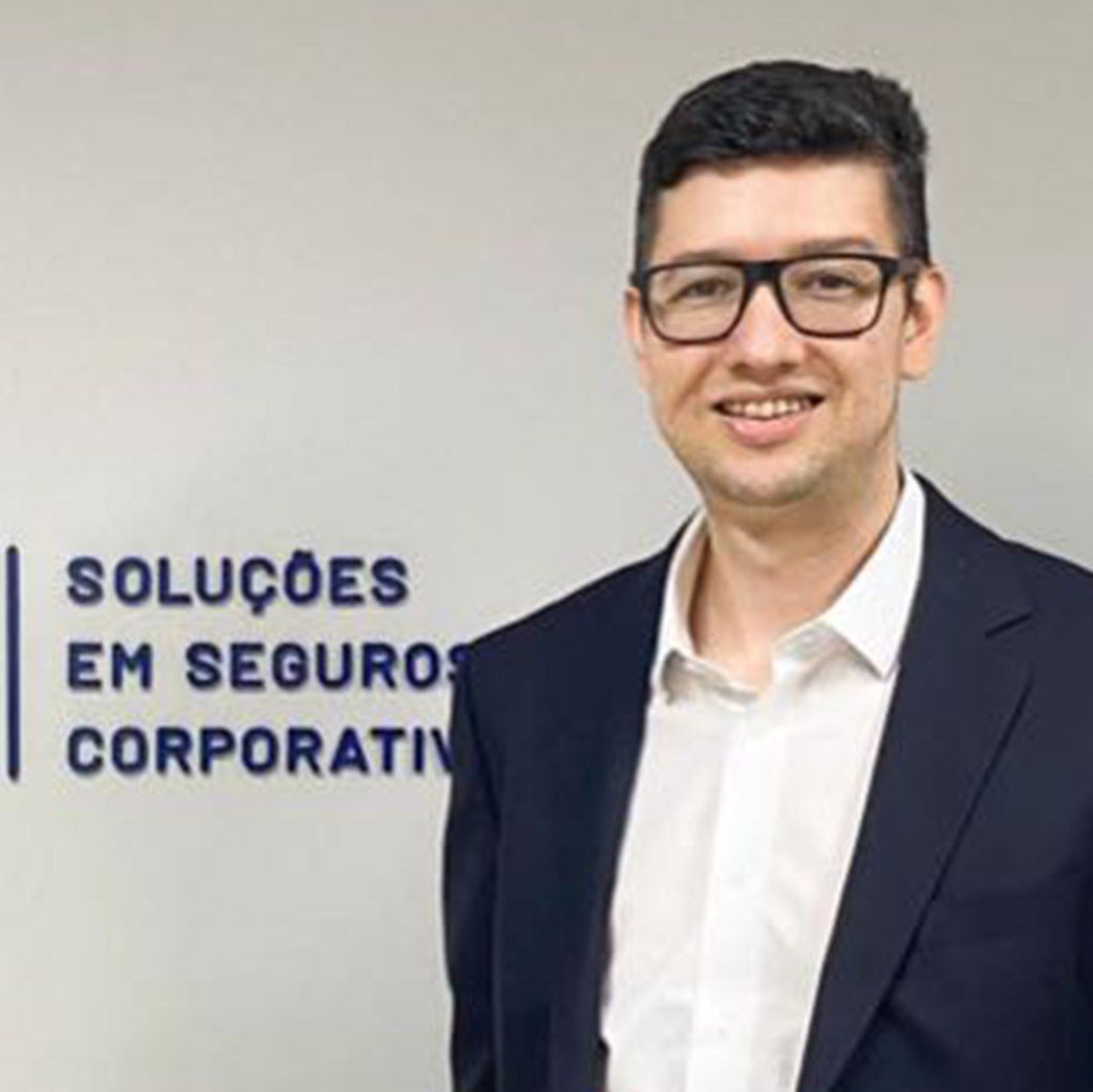 A professional person in a suit and glasses stands before a wall with the text