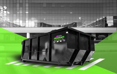 A black dumpster is sitting in a parking lot in front of a building.