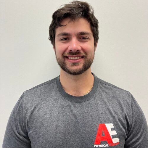 A man wearing a grey nike shirt with the letter a on it is smiling for the camera.