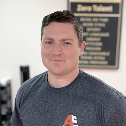 A man in a gray shirt is standing in front of a sign that says zero talent.
